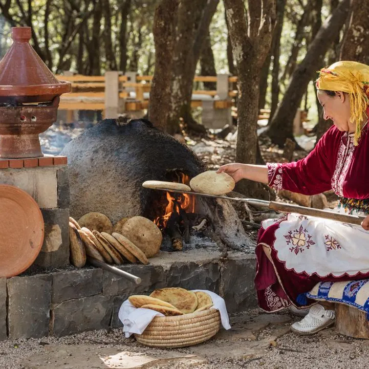 A woman in traditional attire cooks flatbreads over an outdoor wood fire.