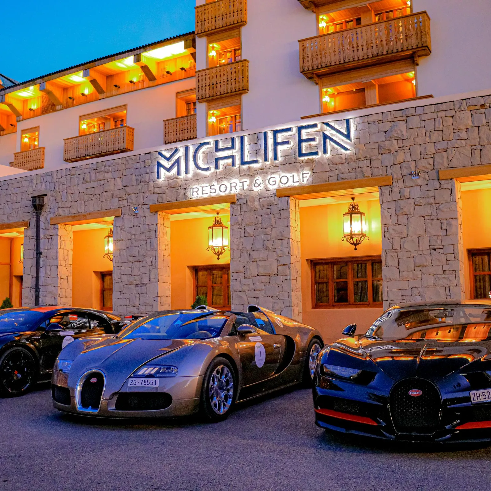 Four luxury cars are parked in front of the illuminated entrance of a hotel named Michlifen Resort & Golf.