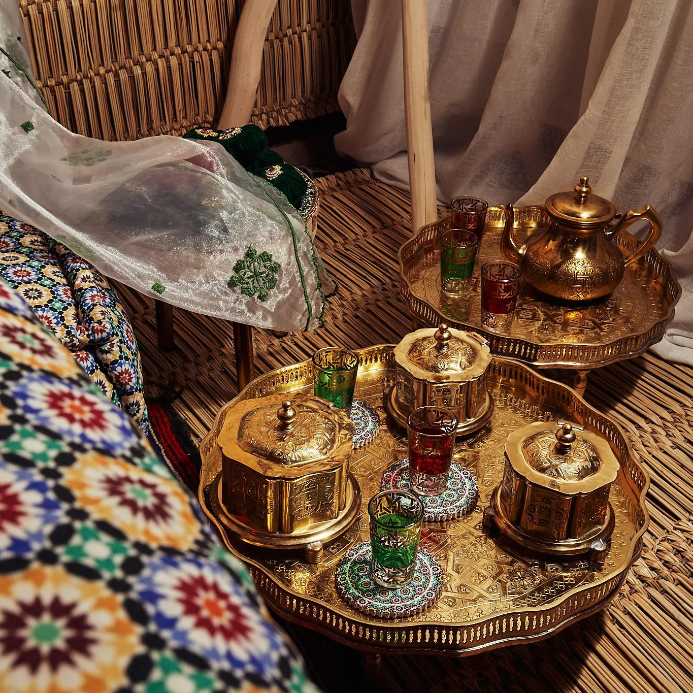 A golden tray with glasses and a teapot is placed on a bamboo table, surrounded by colorful fabrics and curtains.