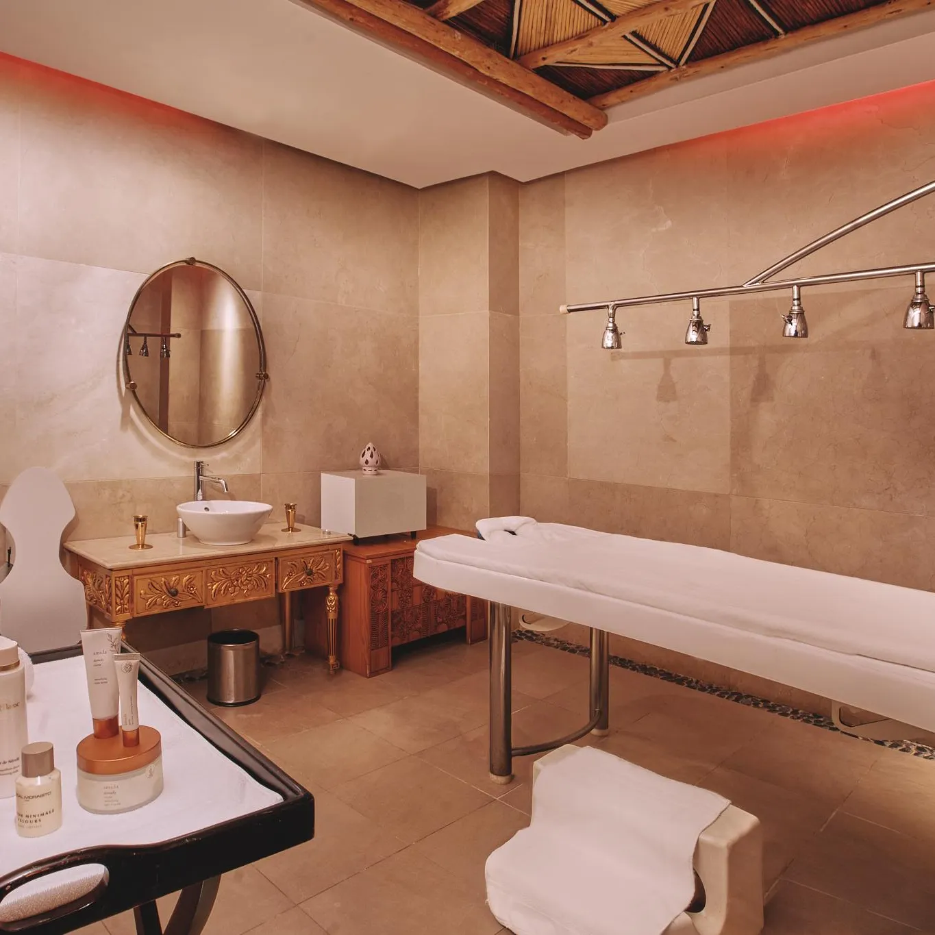 Treatment room with massage table, mirror, sink, and cosmetic products on a table