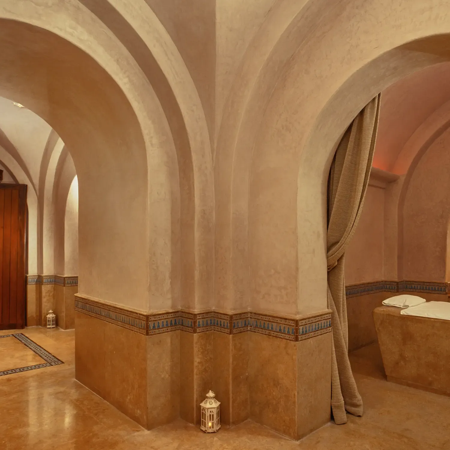 Luxurious bathroom with arches, beige tiling and decorative patterns, containing sinks and a bathtub.