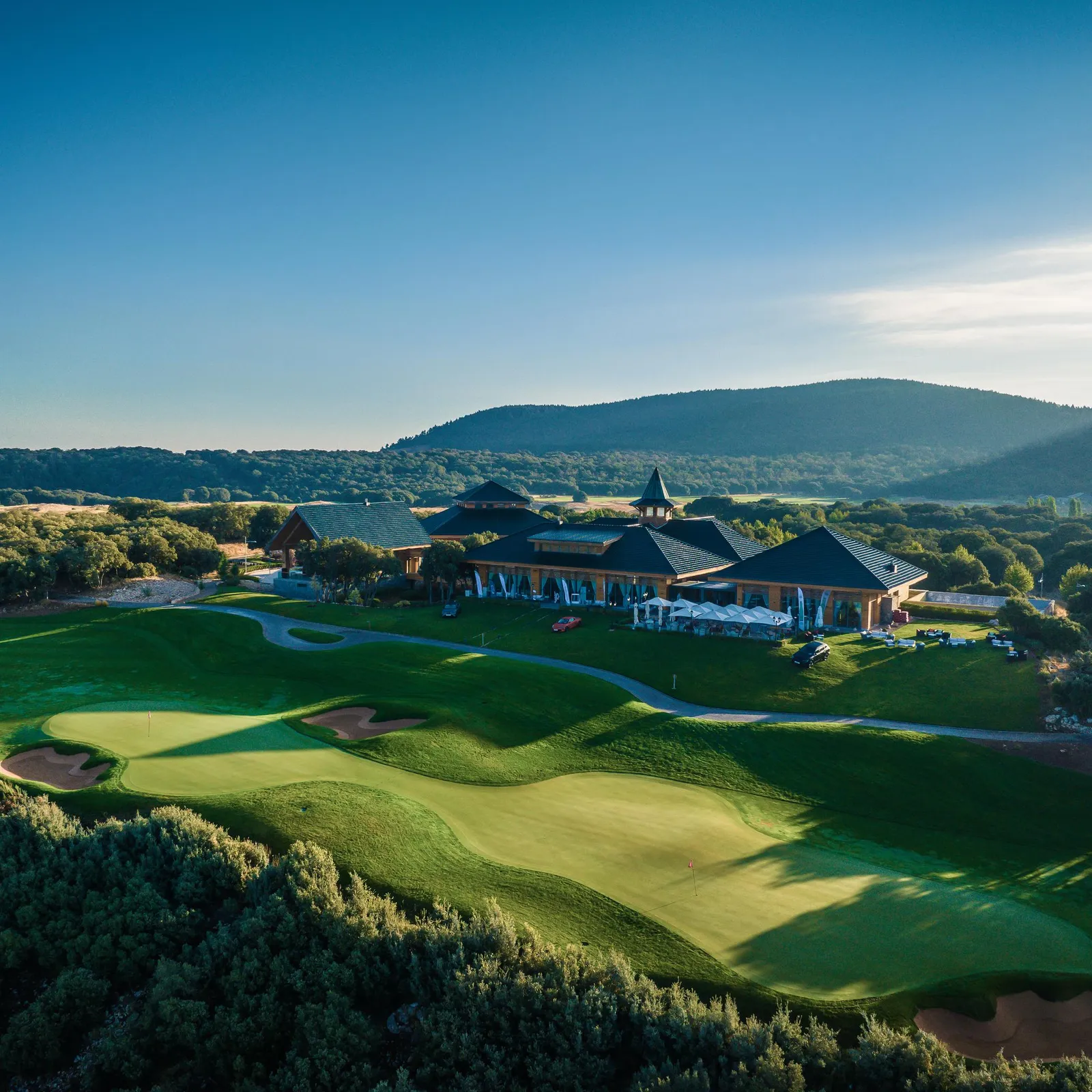 A golf course with a wooden clubhouse and mountains in the background under a clear sky.