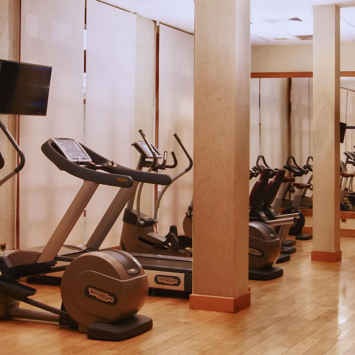 Gym with several cardio-training machines, including ellipticals and bikes, lined up against a wall with mirrors