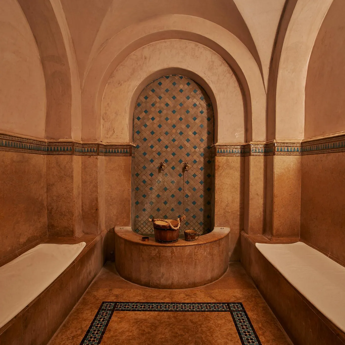 Hammam room with stone benches, a tiled niche with geometric patterns, and metal buckets