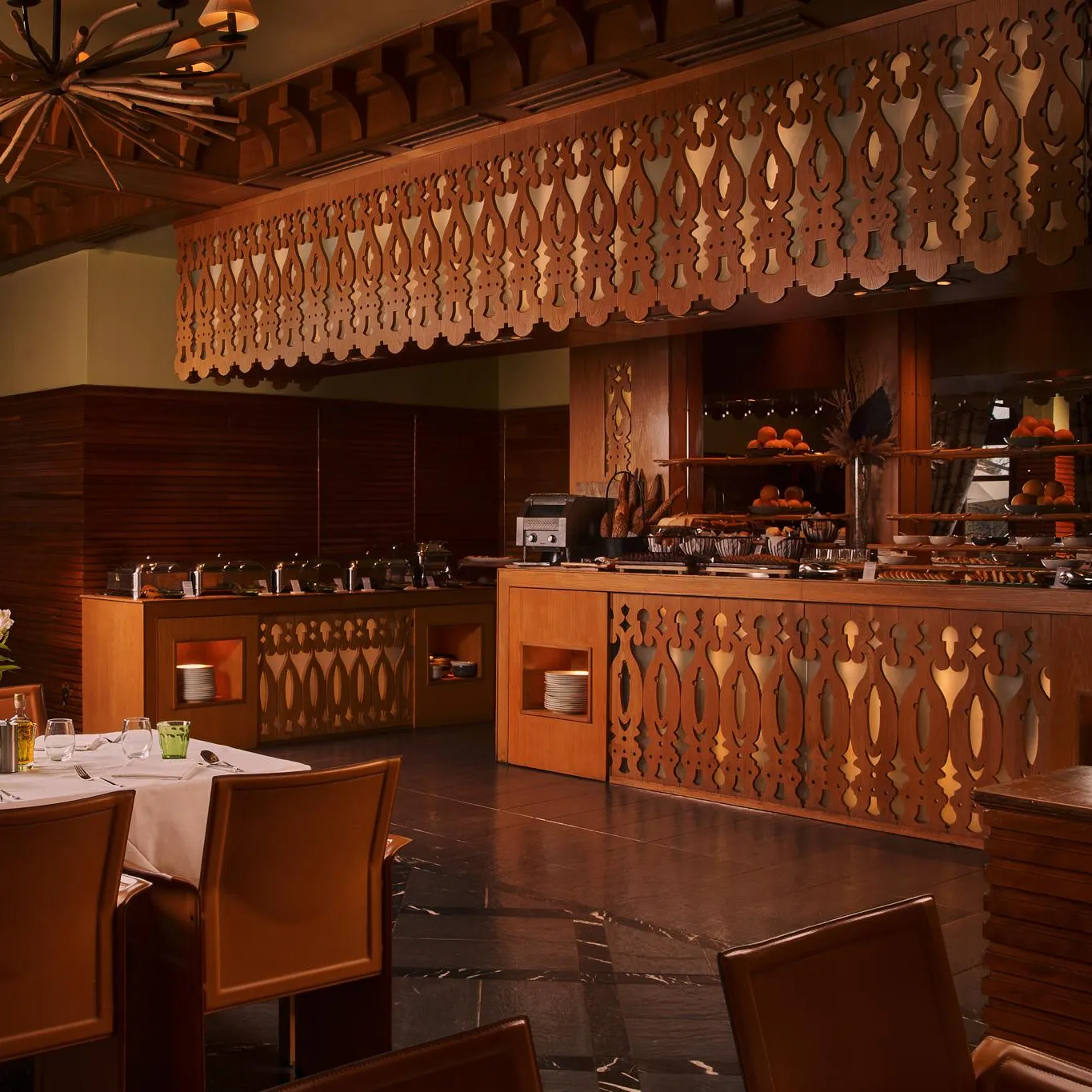 Restaurant with tables set and a pastry buffet, decorated with wood and lit by hanging lamps.