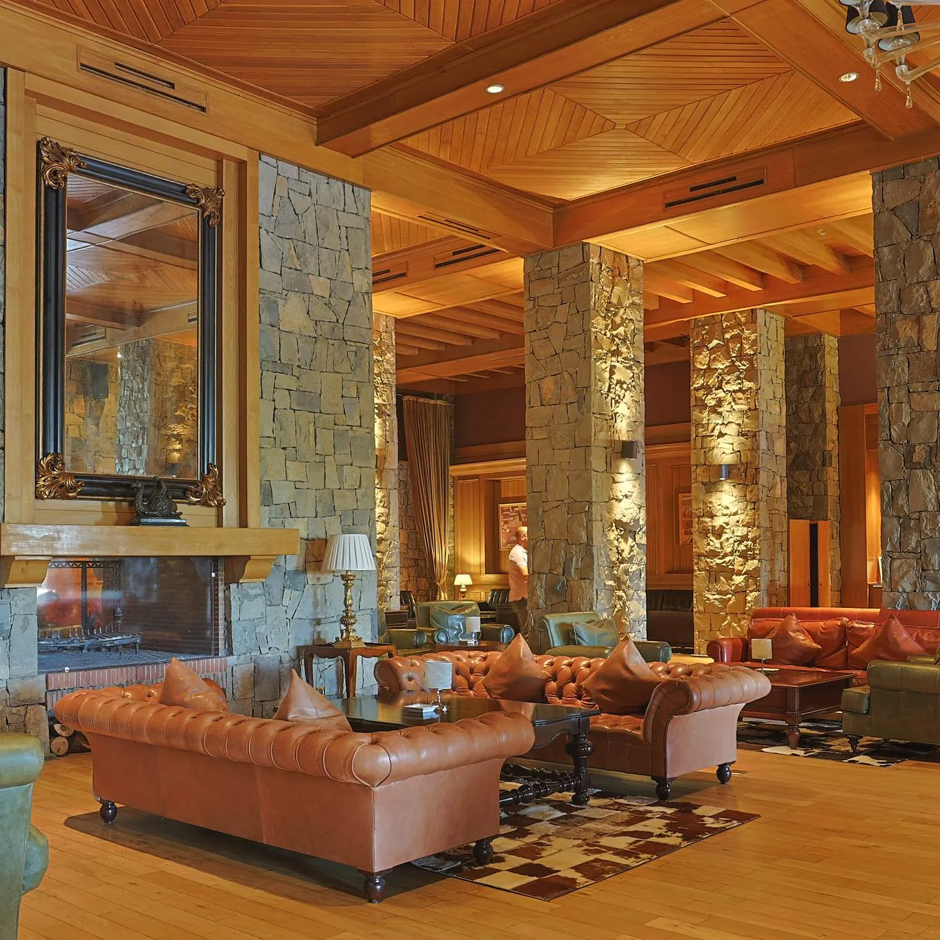 A large lounge with leather sofas, stone columns, and a bar at the back