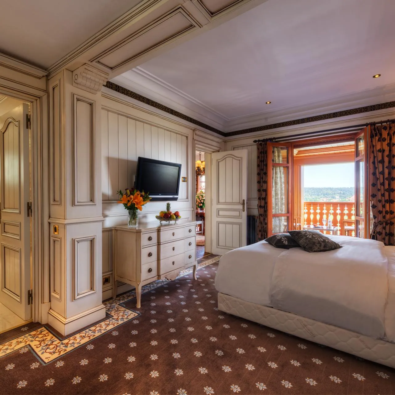 Luxurious room with double bed, television, dresser, balcony view and open door to bathroom