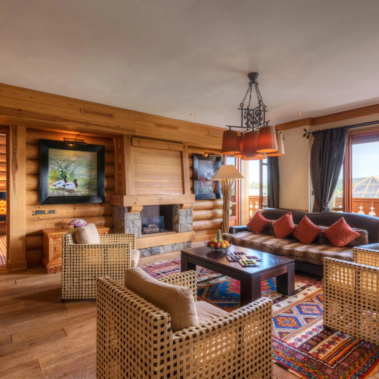 Wooden lounge with sofa, rattan armchairs, coffee table, fireplace and large window