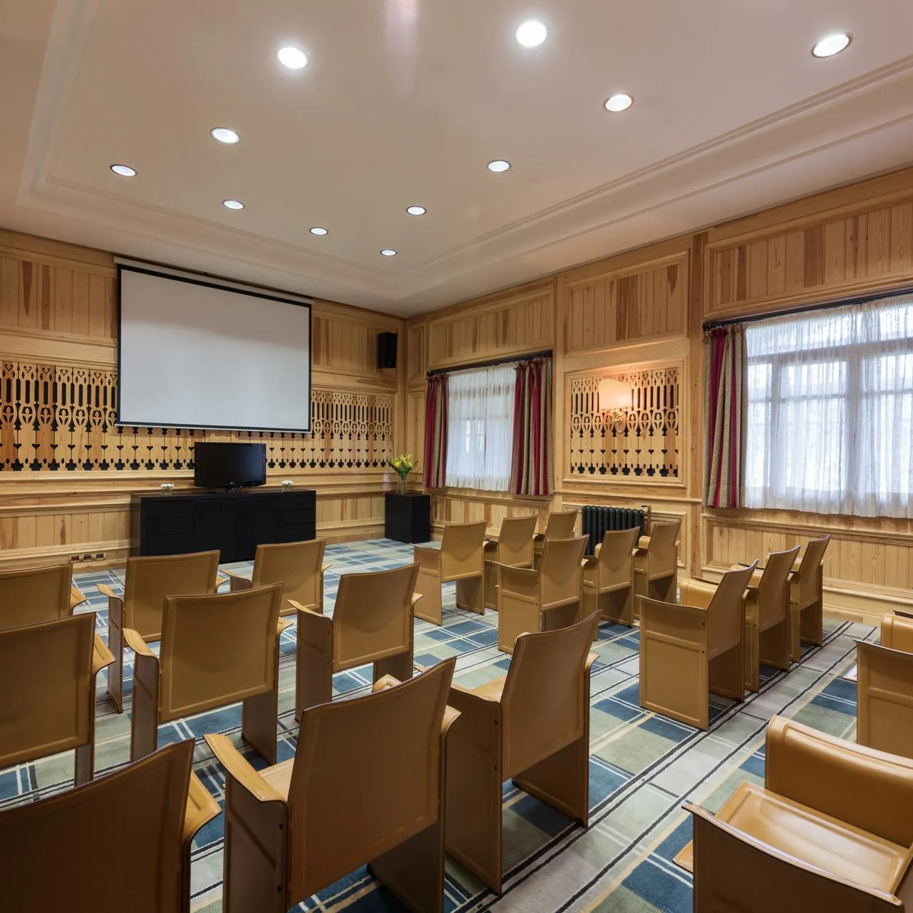 Meeting room with wooden chairs, a projection screen, a projector, and windows with curtains.