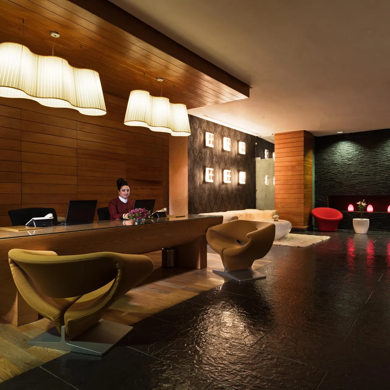 Modern hotel reception with a glass reception desk, colorful seating, and suspended lighting fixtures