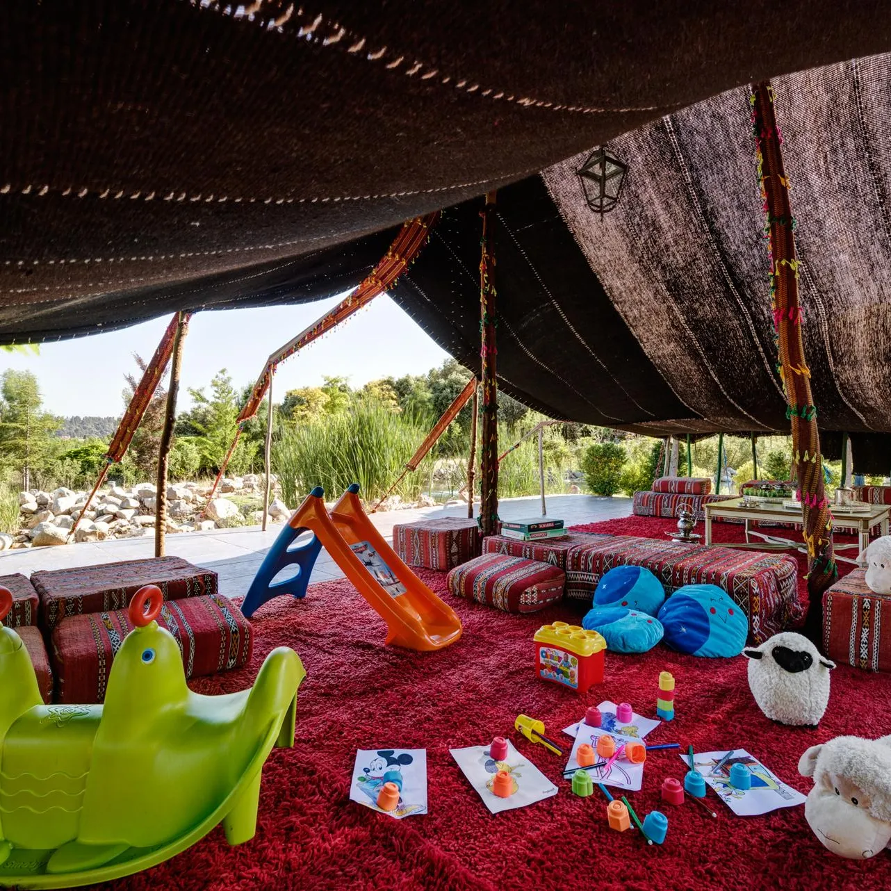 A covered space with children's toys, cushions, and colorful decorations, surrounded by vegetation.