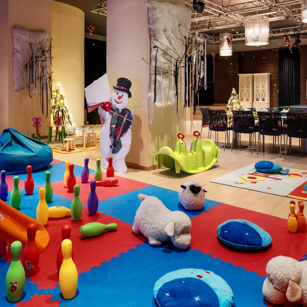 Children's playroom with a cardboard snowman, colorful skittles, cushions, and toys on red and blue mats