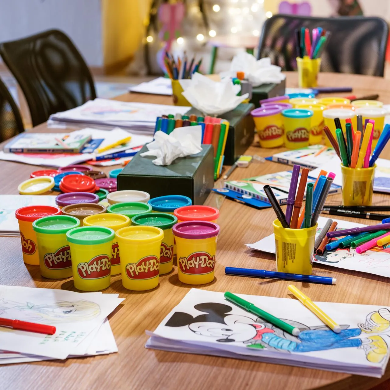 Table with drawing materials, Play-Doh clay pots, and colored sheets