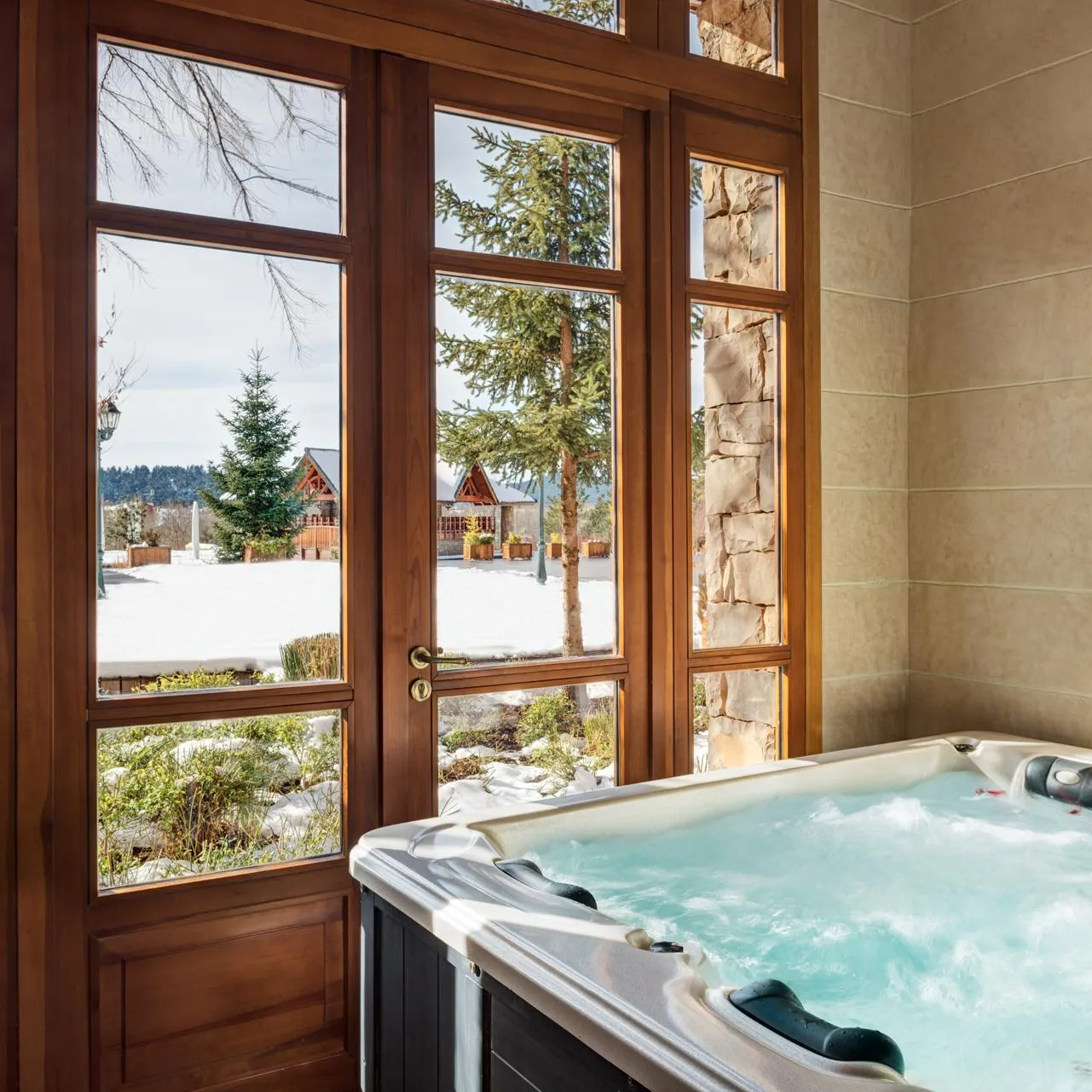 Jacuzzi filled with water with a view of a snowy landscape through large wooden windows