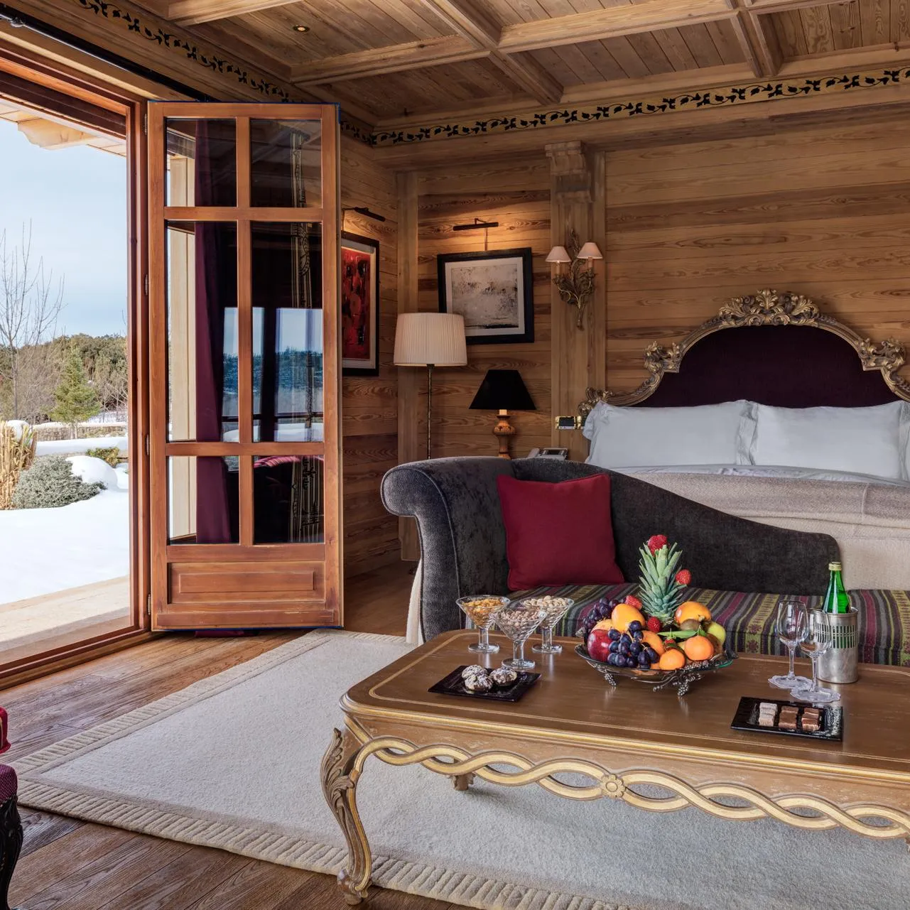 Wooden room with four-poster bed, chair, coffee table with fruit and glasses, view of snowy exterior