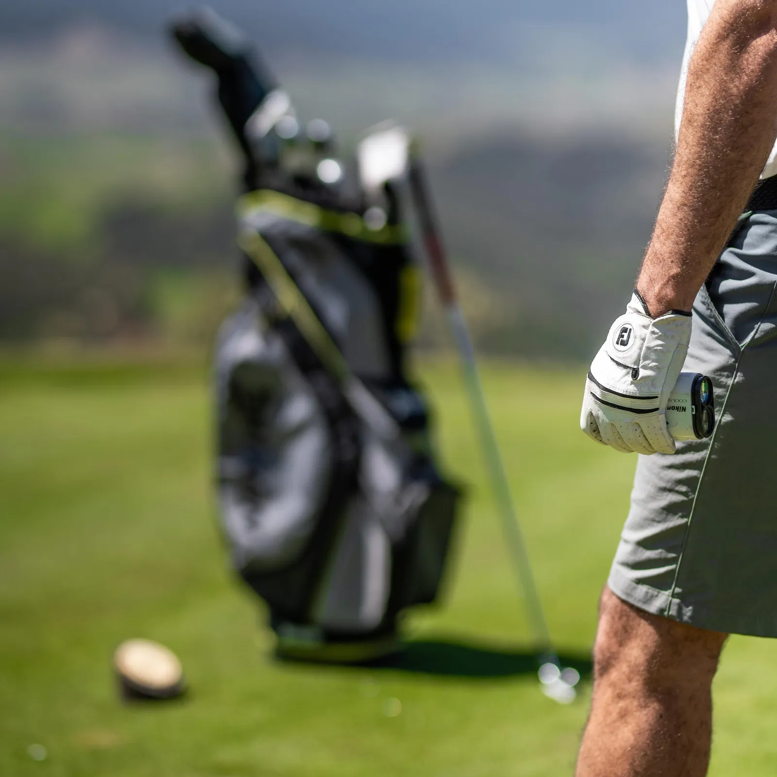 A golfer in action with a bag of clubs in the background and a golf ball on the ground