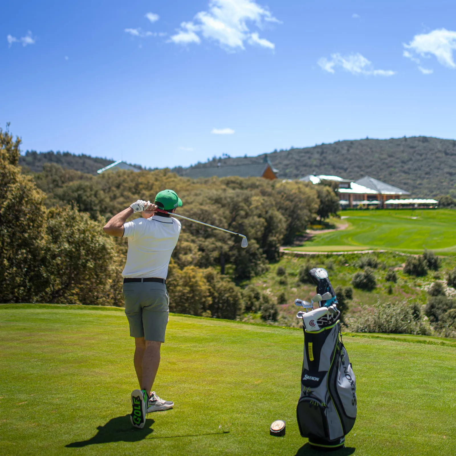 A golfer hitting a ball on a golf course with a bag of clubs nearby