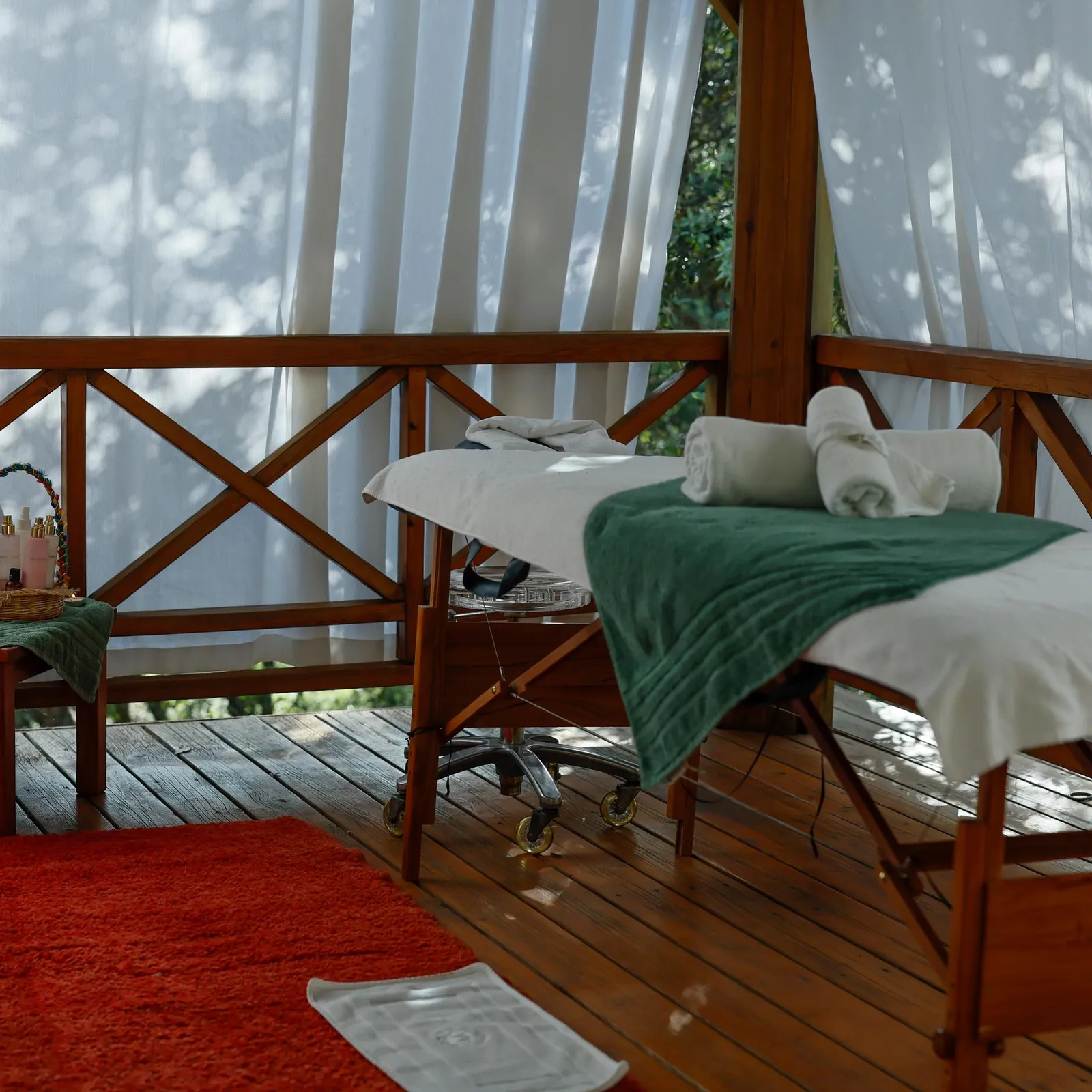 Two wooden massage tables with towels and products on a wooden terrace surrounded by white curtains