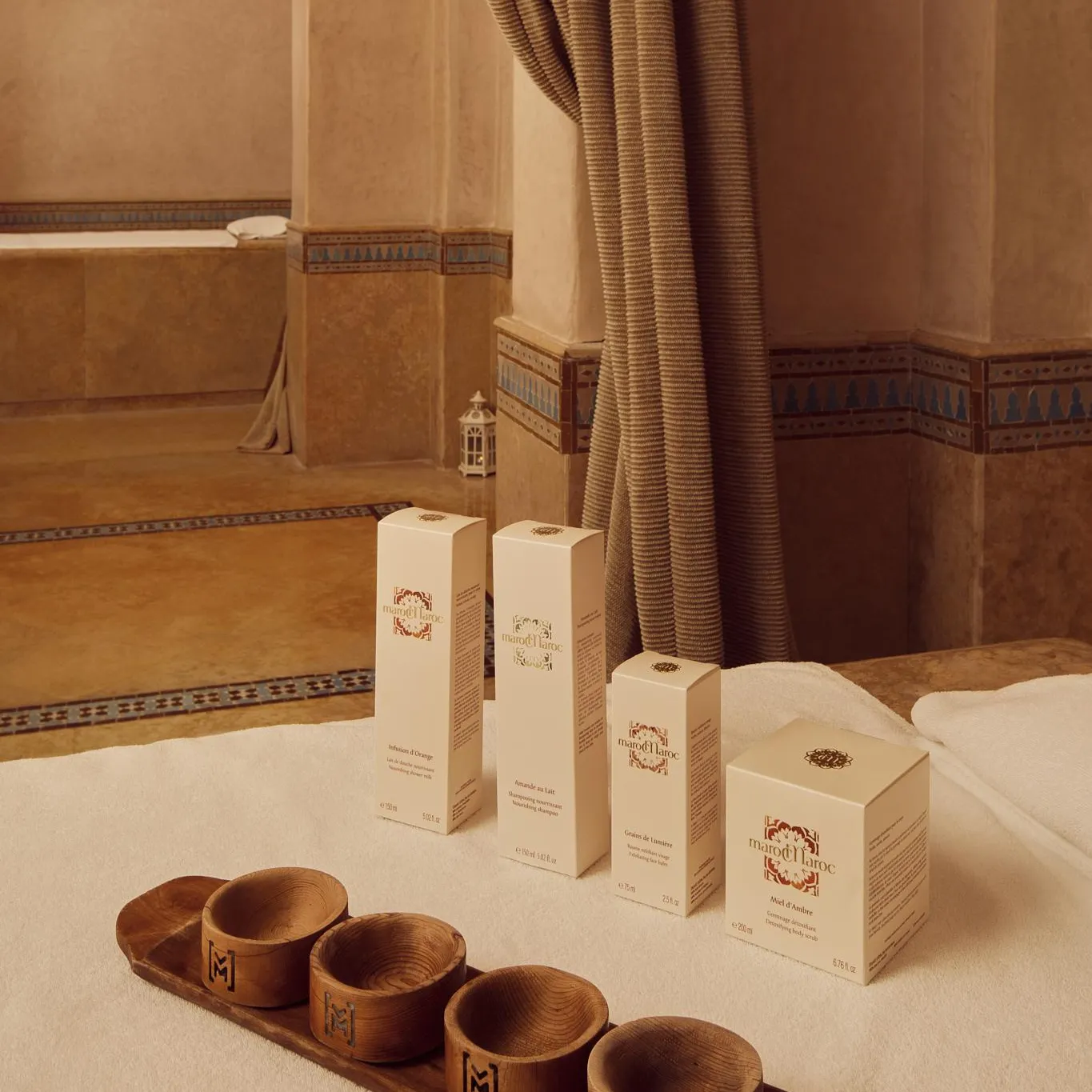 Four boxes of cosmetic products and a wooden tray with small dishes placed on a white rug in a room with ceramic-tiled walls.