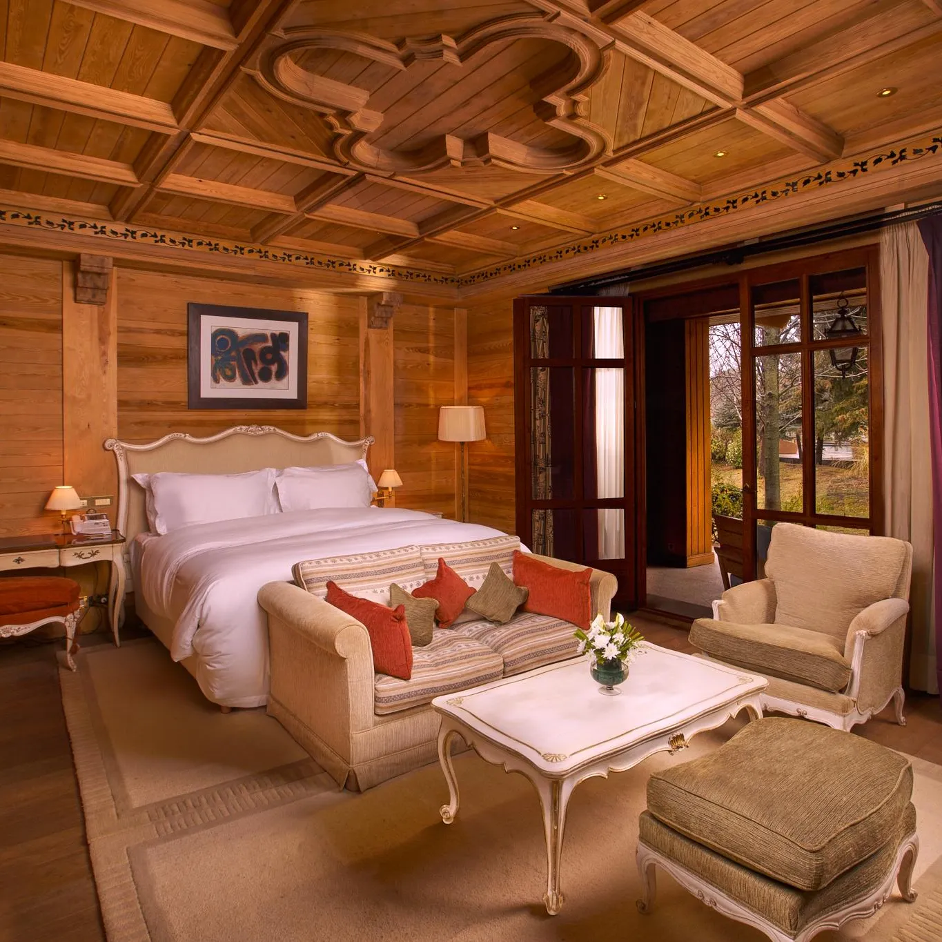 Wooden room with double bed, sofa, armchairs, coffee table and windows overlooking the outside.