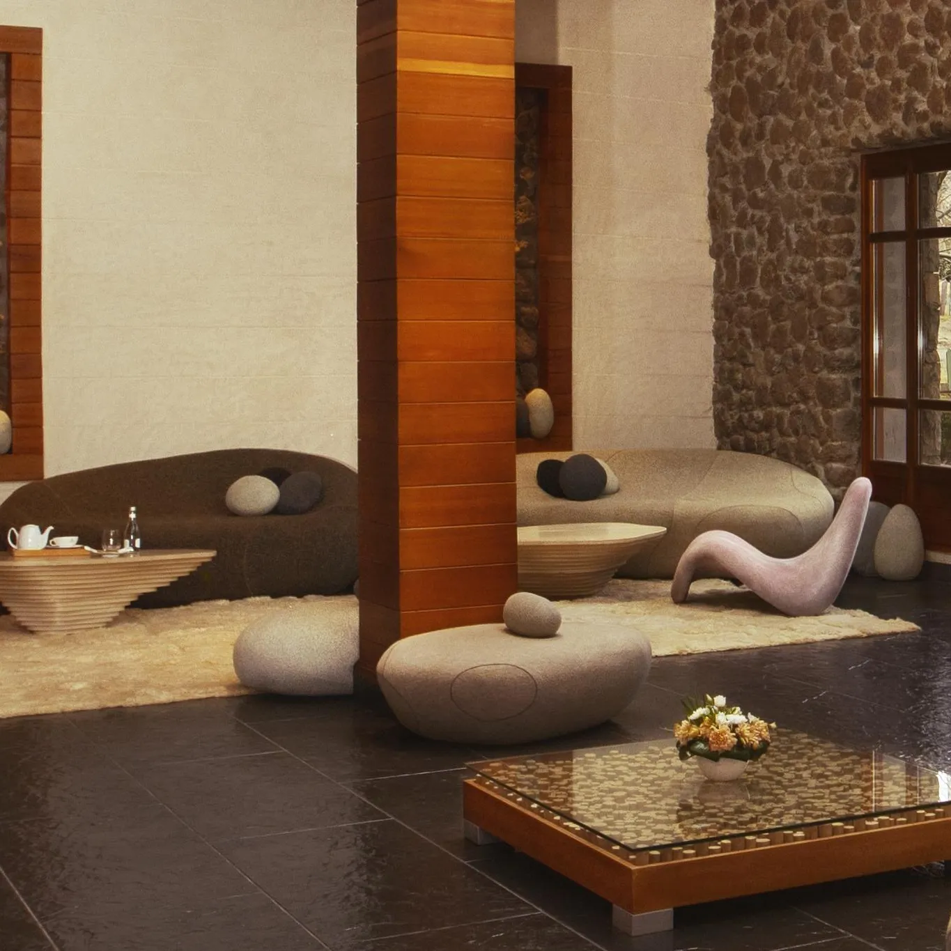 Lounge area with cushions and rock-shaped seats, low tables, and stone walls with windows.