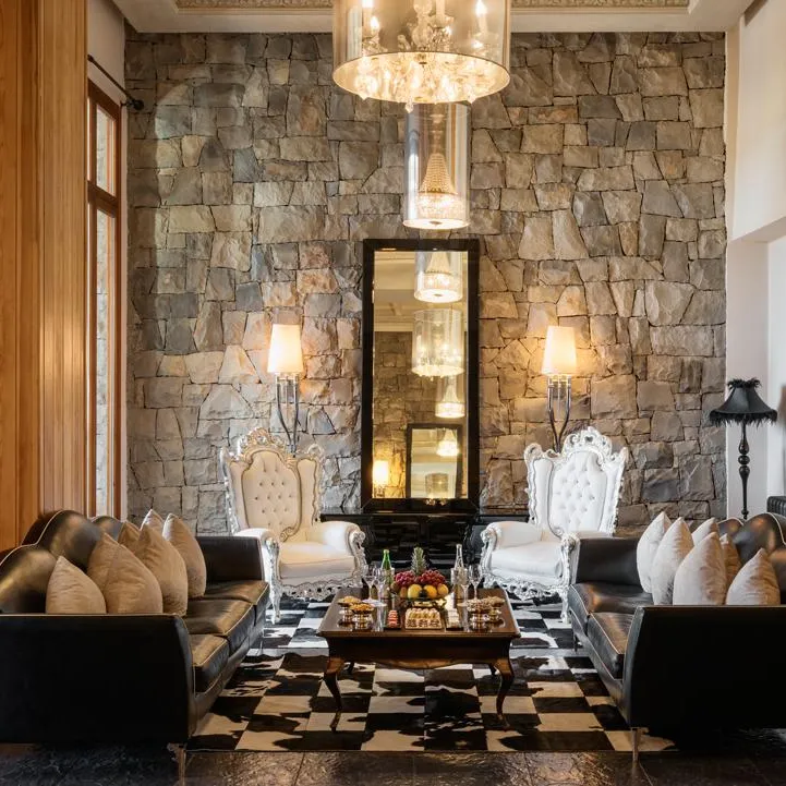 Living room with black sofas, white armchairs, coffee table, and stone fireplace, lit by lamps and a chandelier.