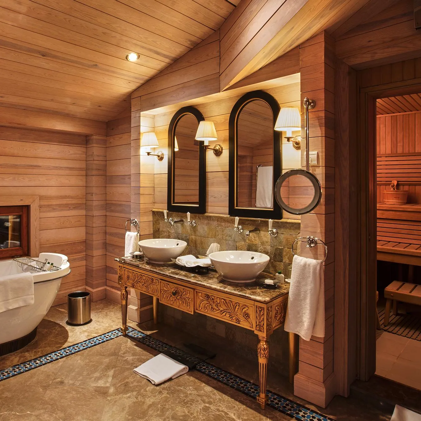 Wooden bathroom with bathtub, double sink, mirror, and open door to a sauna.