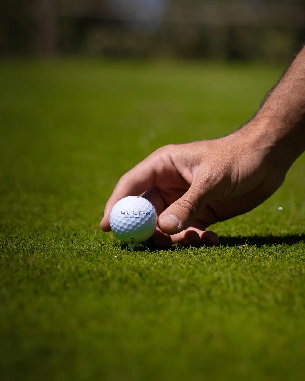 A hand places a golf ball on a tee on green grass.