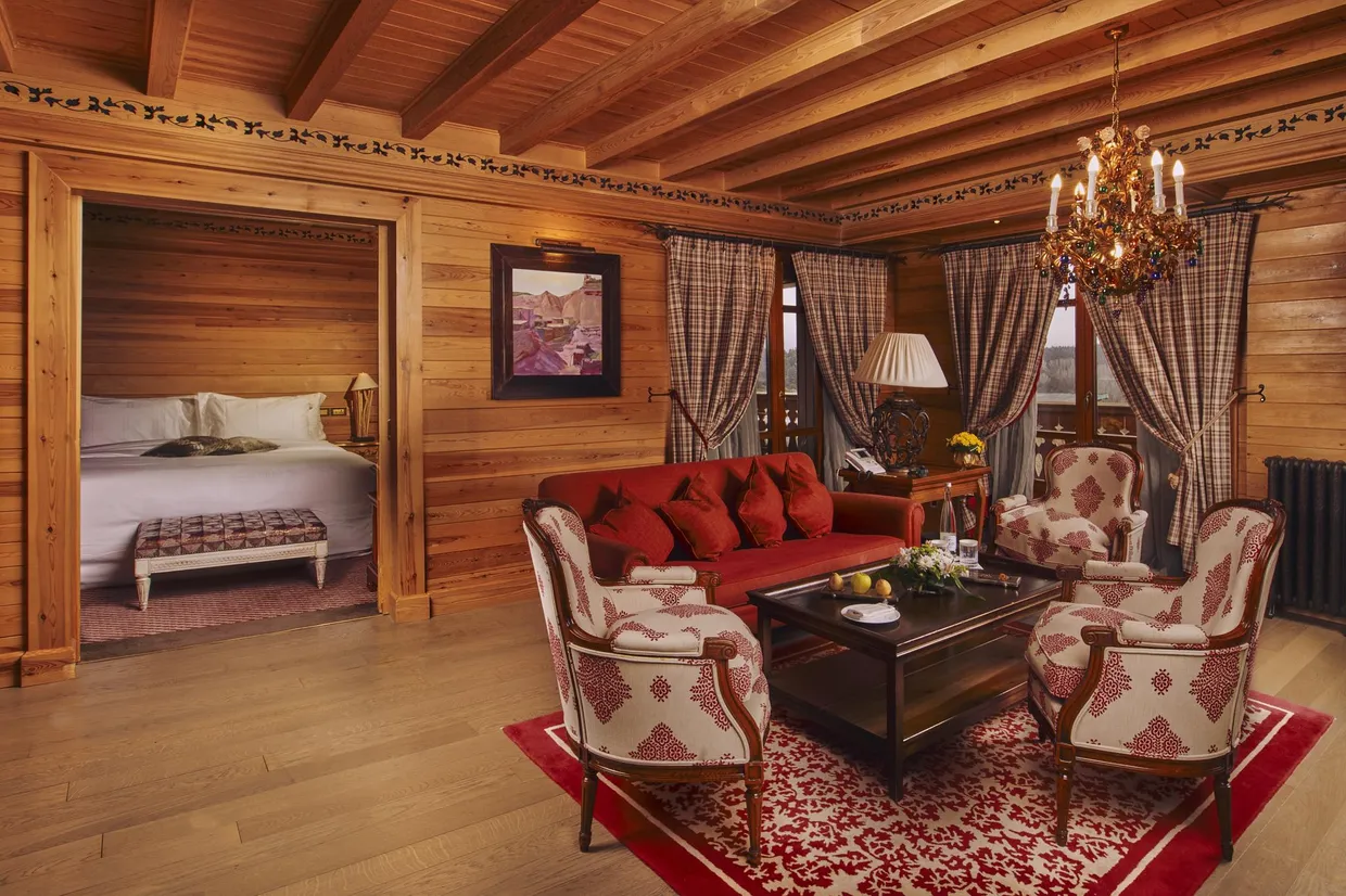 Chambre en bois avec lit, canapé rouge, fauteuils et chandelier suspendu