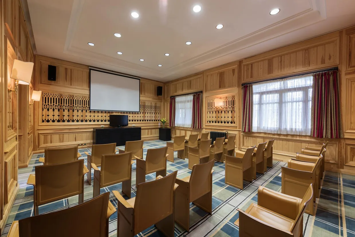 Meeting room with wooden chairs, a projection screen, a projector, and windows with curtains.