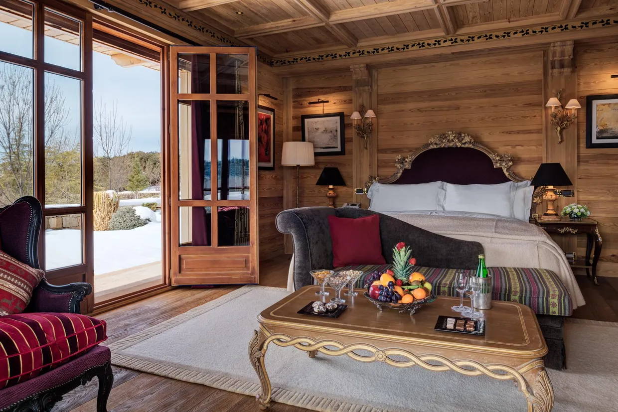 Chambre en bois avec lit à baldaquin, chaise, table basse avec fruits et verres, vue sur l'extérieur enneigé