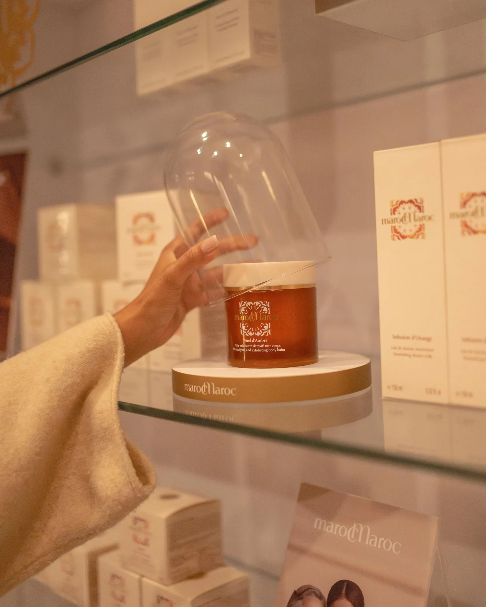 A hand holding a glass of wine in front of a display of MarocMaroc cosmetics