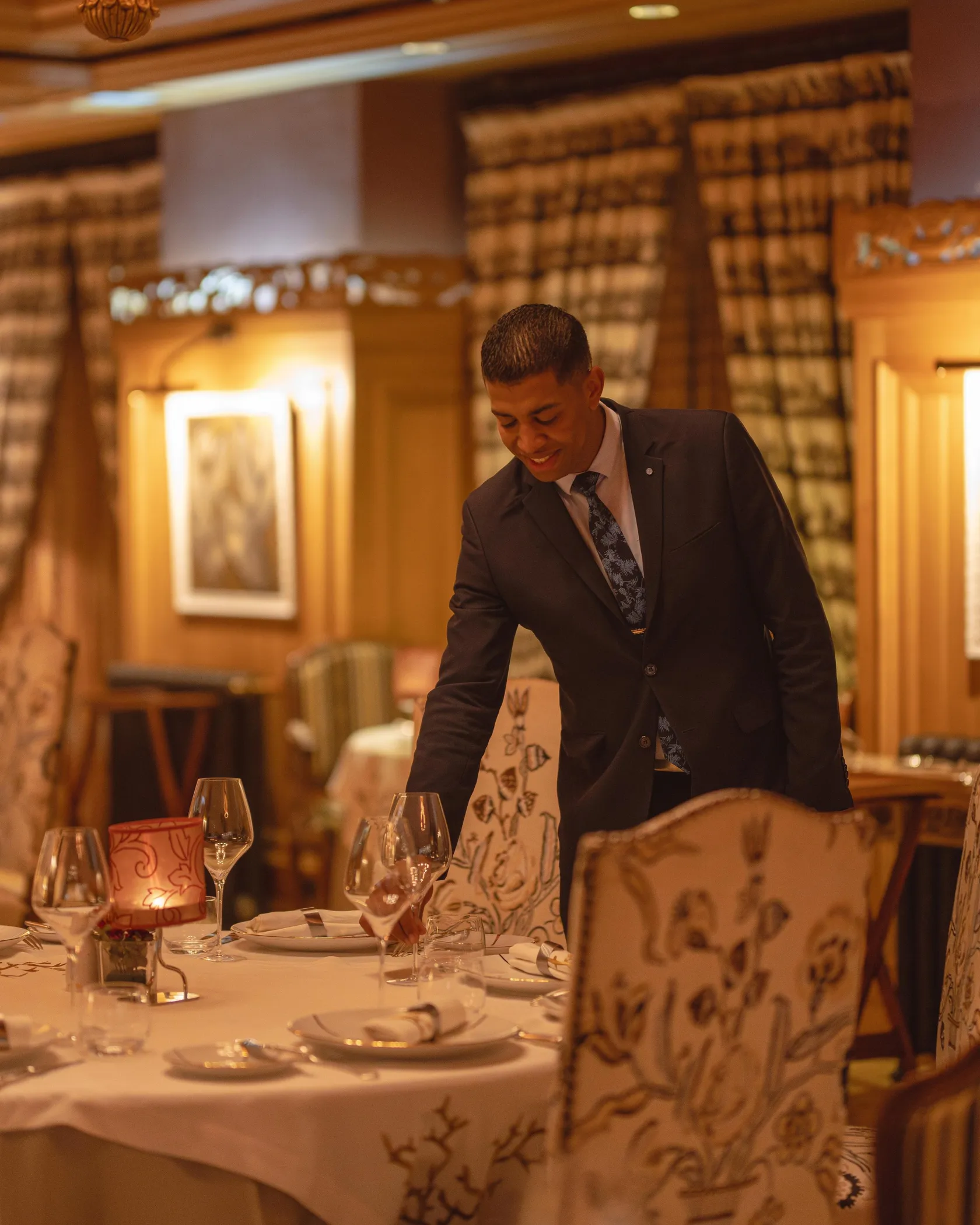 Un serveur en costume noir s'occupe d'une table dressée dans un restaurant à l'ambiance chaleureuse