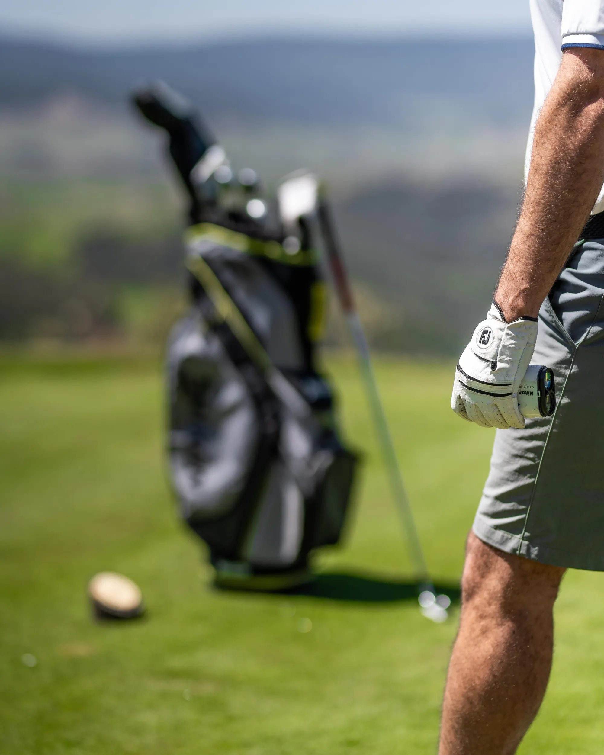 A golfer in action with a bag of clubs in the background and a golf ball on the ground