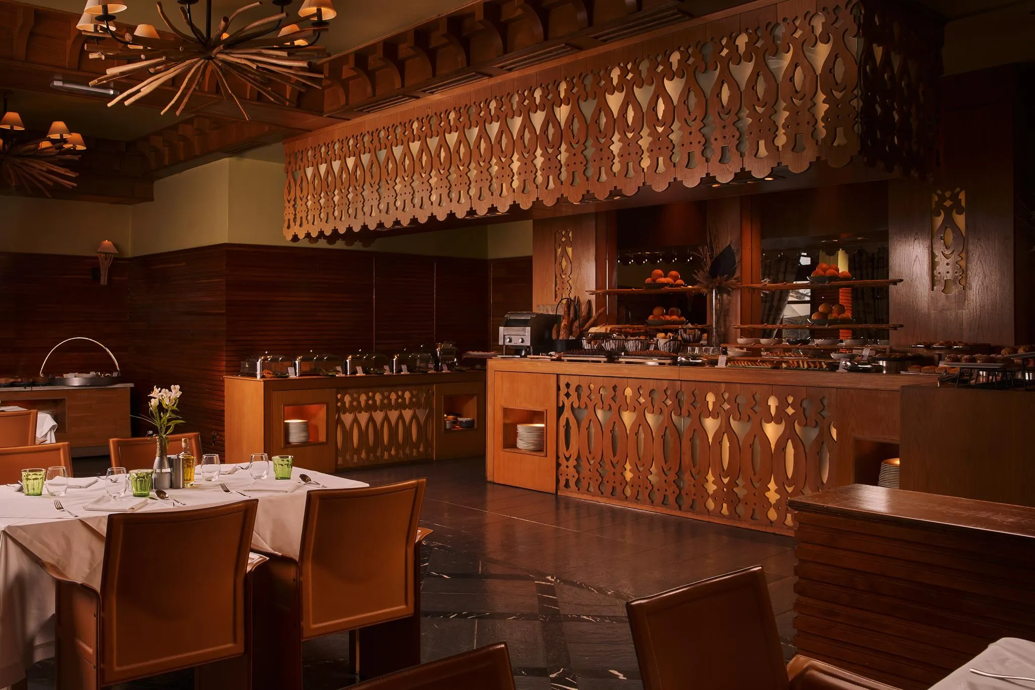 Restaurant avec des tables dressées et un buffet de pâtisseries, décoré de bois et éclairé par des lampes suspendues