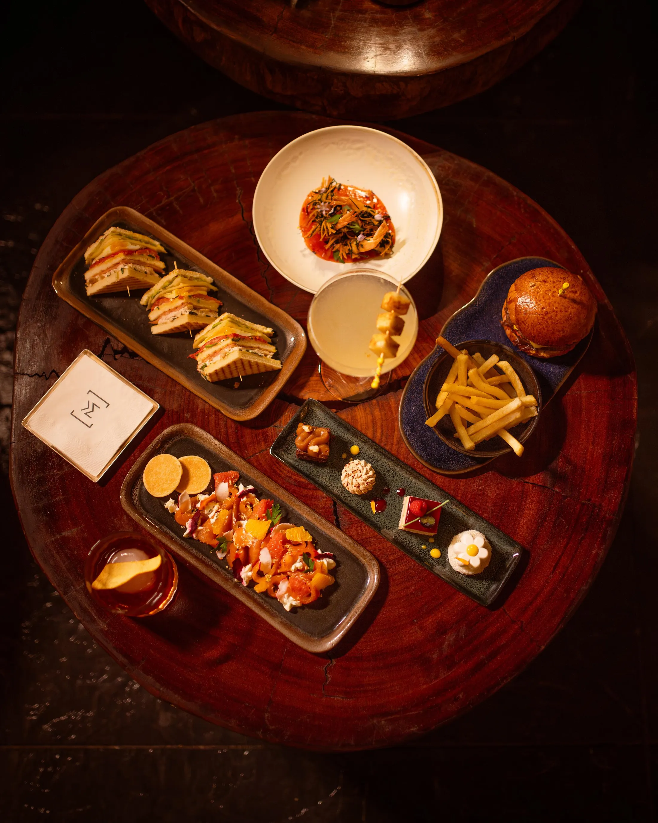 Un plateau de nourriture variée incluant des sandwichs, des frites, une soupe, des amuse-gueules et des desserts sur une table en bois