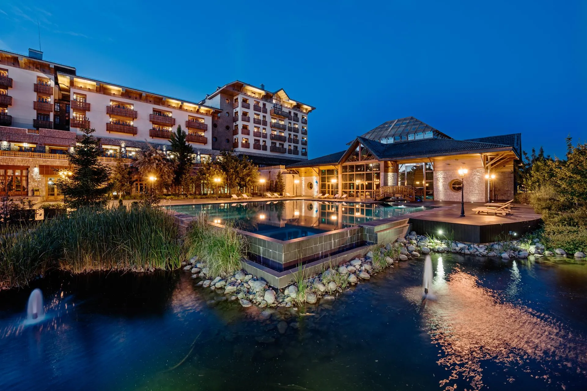 A hotel complex with a pool and illuminated fountains in the evening