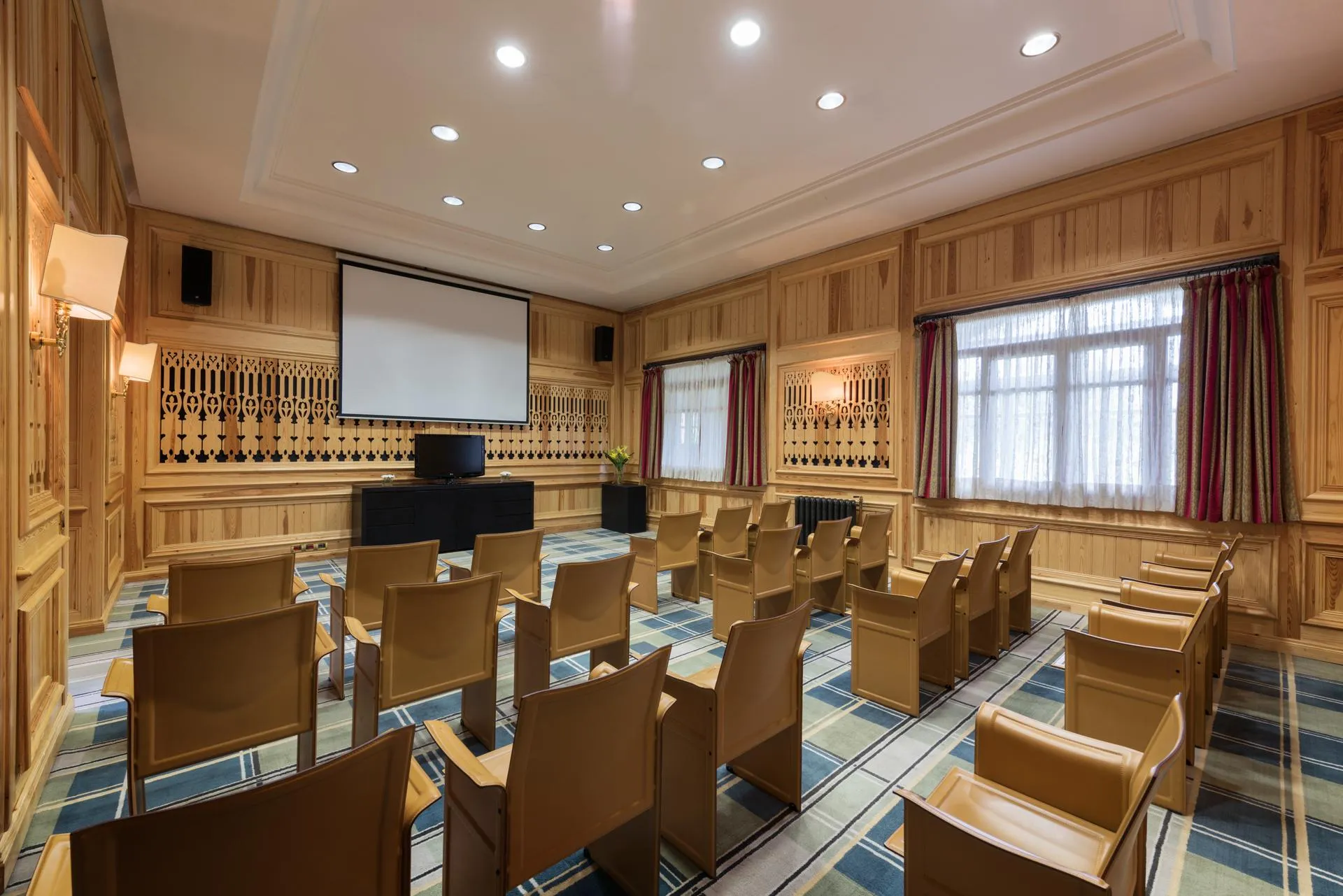 Meeting room with wooden chairs, a projection screen, a projector, and windows with curtains.