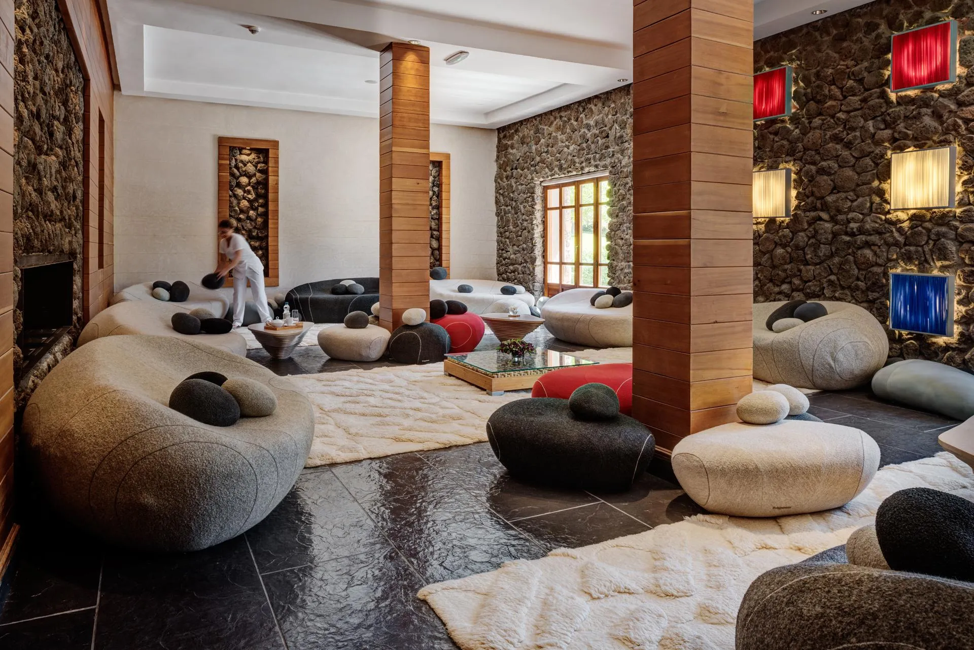 A person in white clothing is cleaning the floor of a room with giant cushions and stone and wood walls.