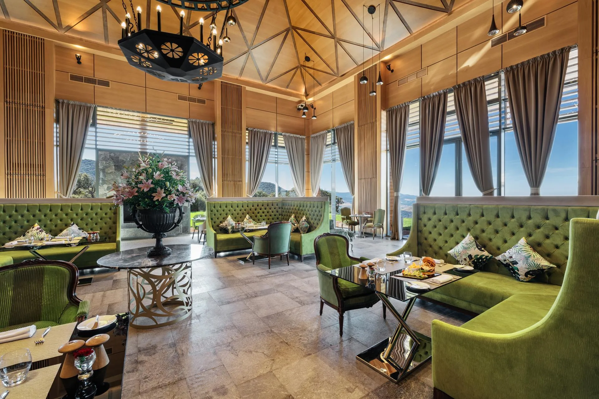 An elegant restaurant with green banquettes, set tables, and large windows offering a panoramic view.