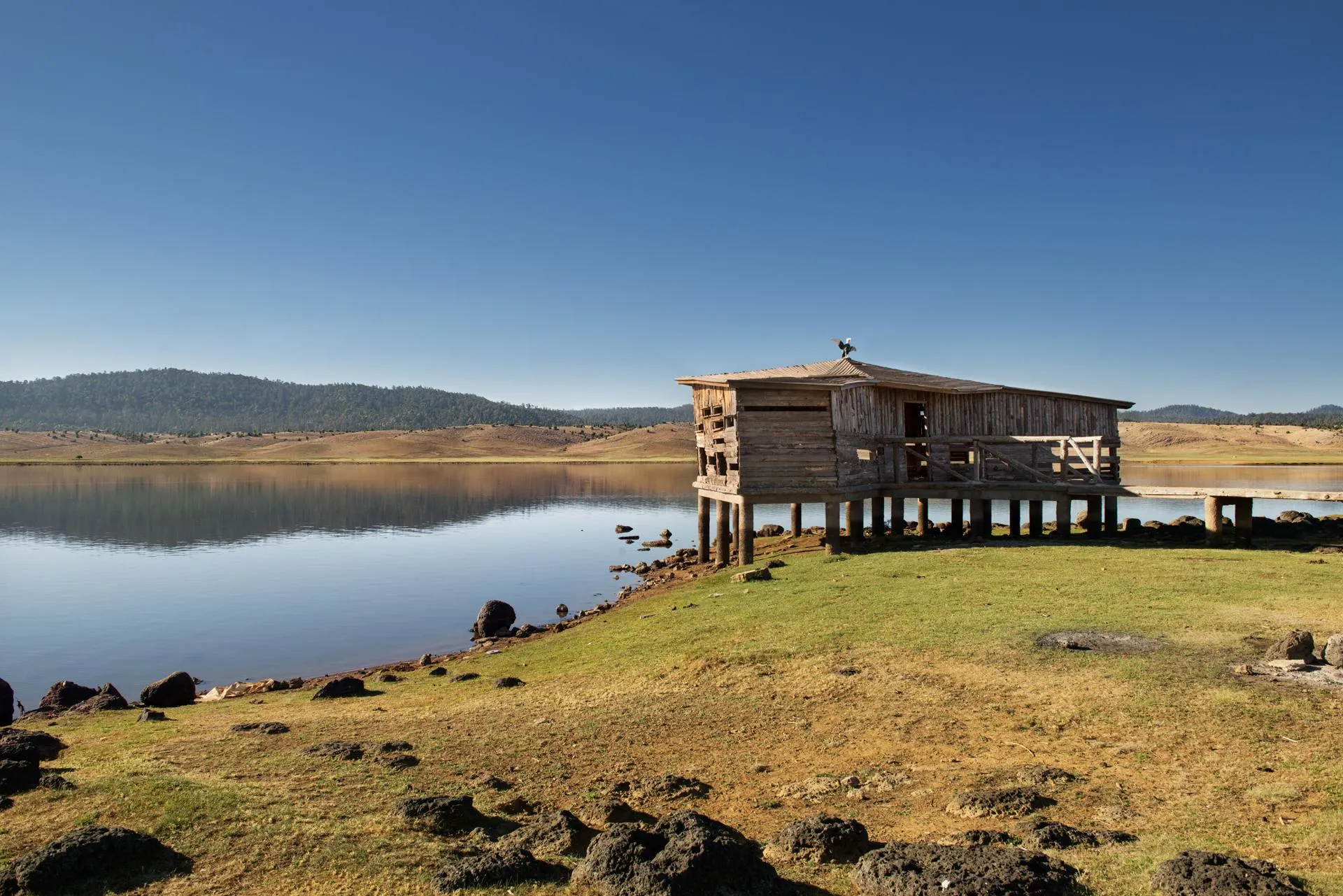 A wooden cabin on stilts by a lake with mountains in the background