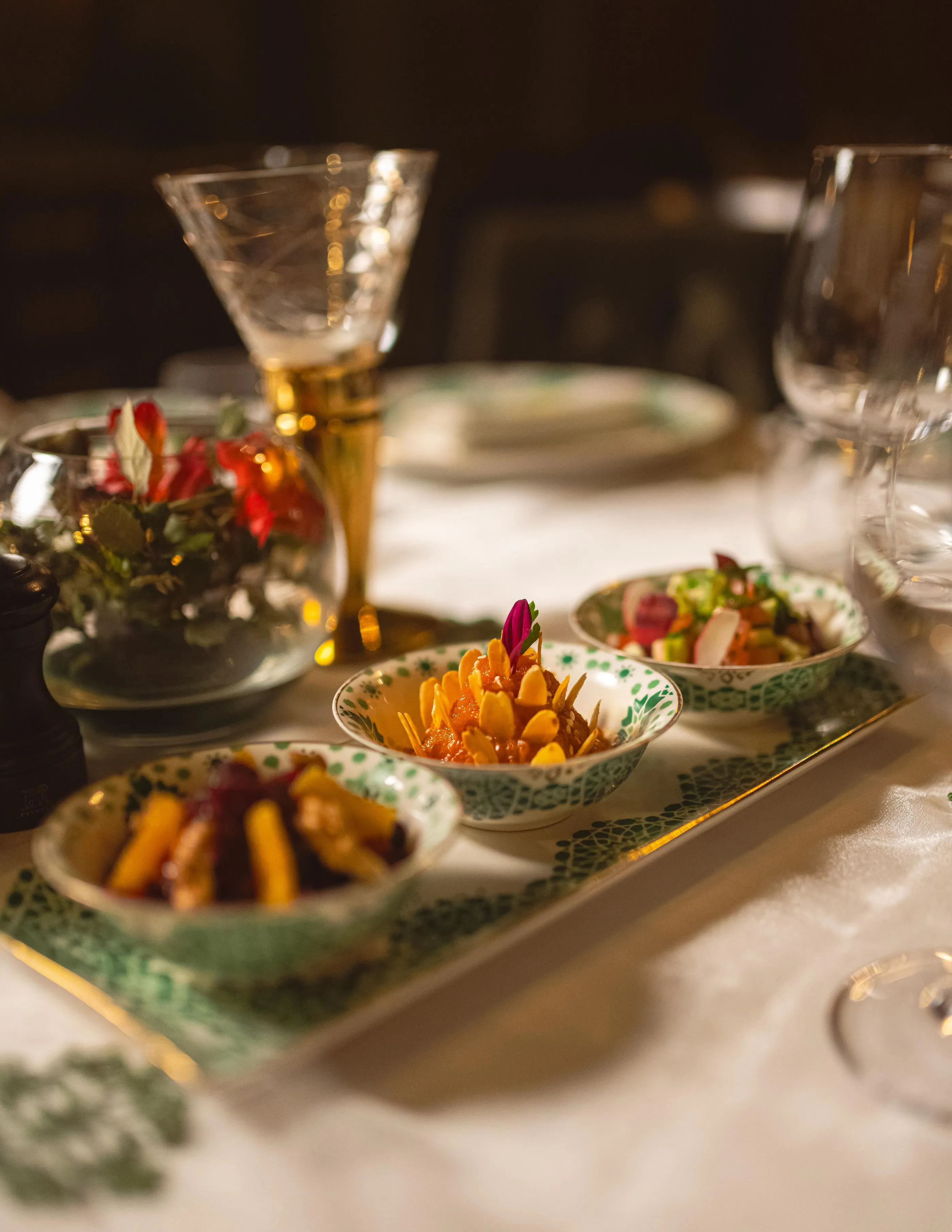 Plates of small dishes filled with vegetables and flowers, accompanied by cocktail glasses on a table