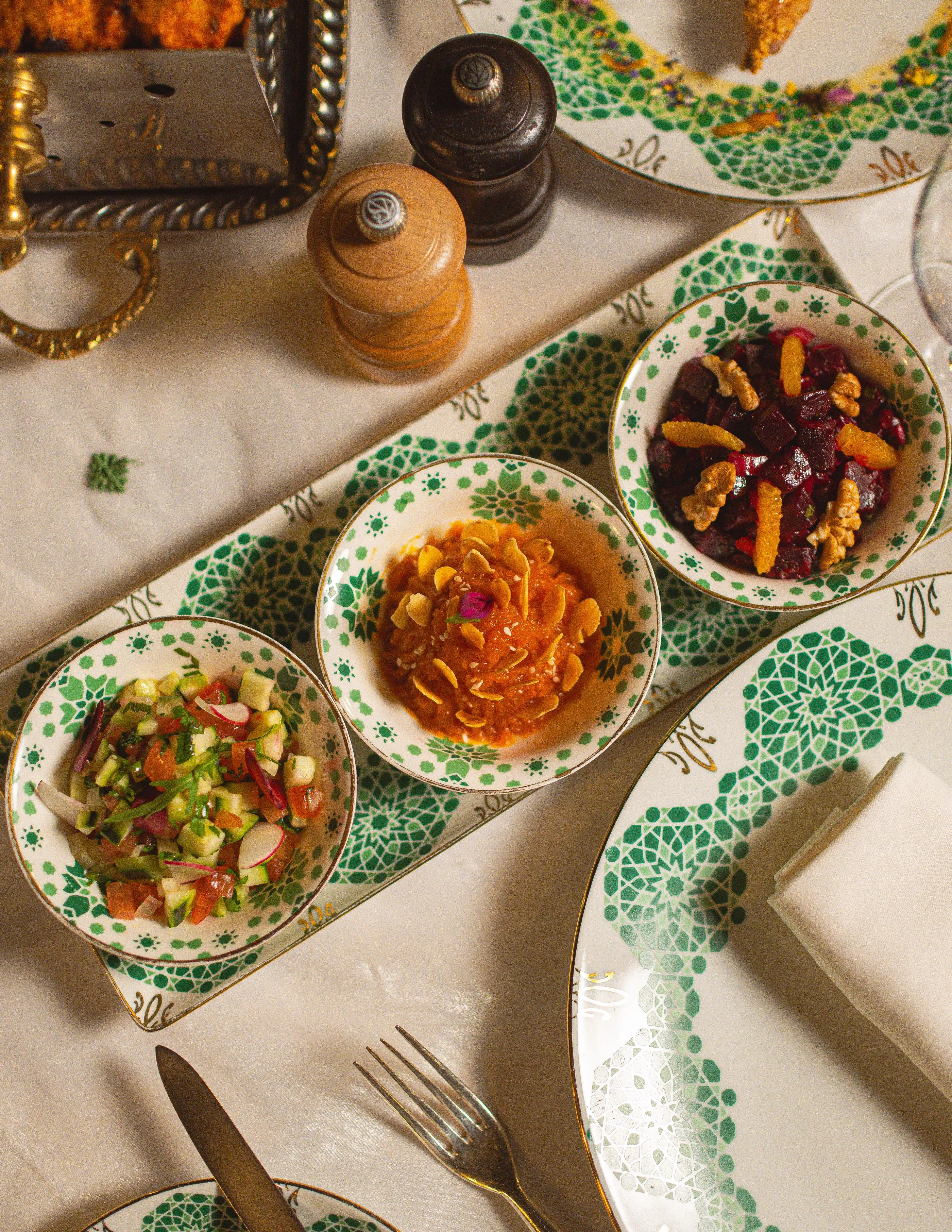 Three small bowls of colorful food on a table with cutlery and spices