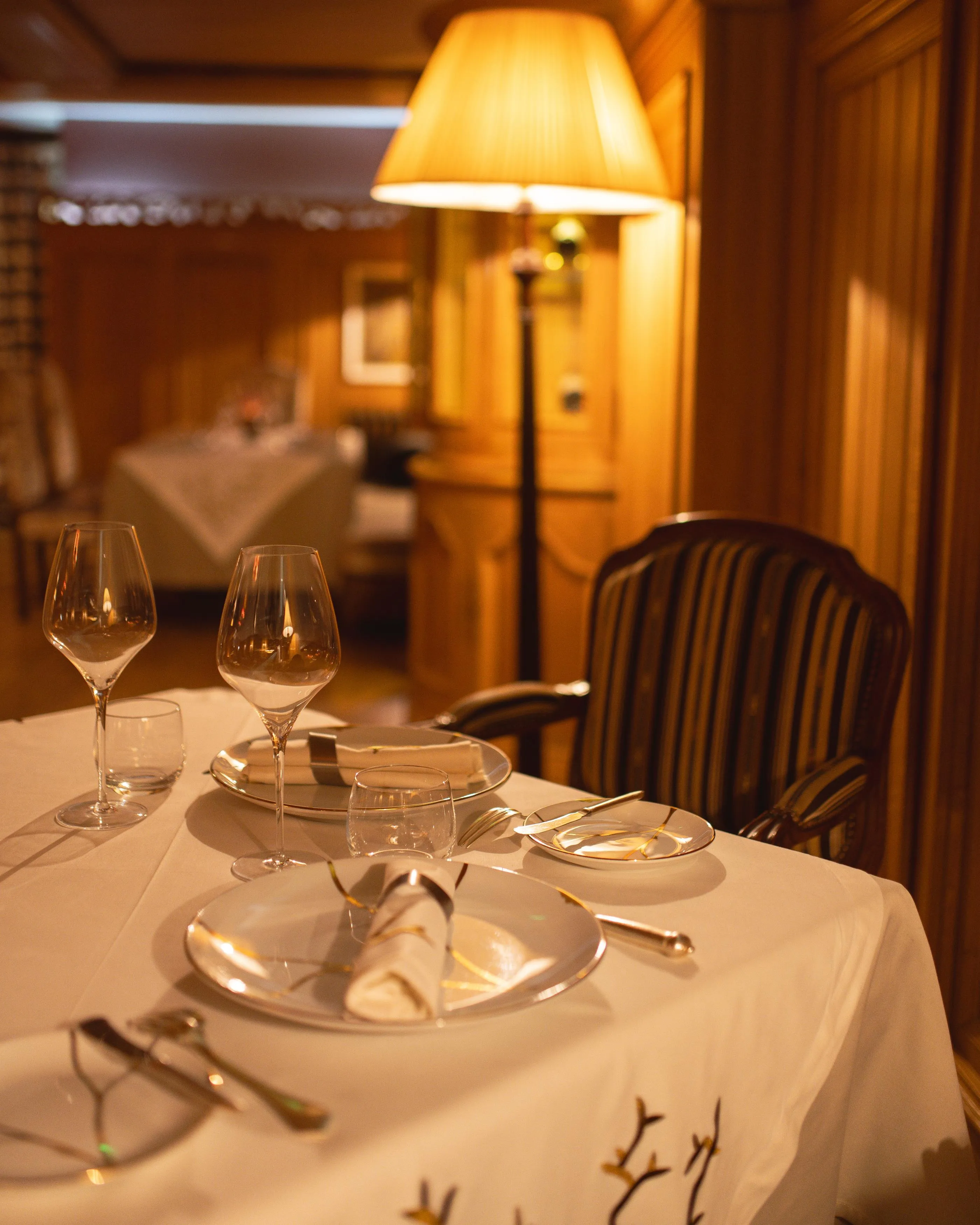 Table dressée avec verres à vin, couverts et nappe blanche dans un restaurant faiblement éclairé