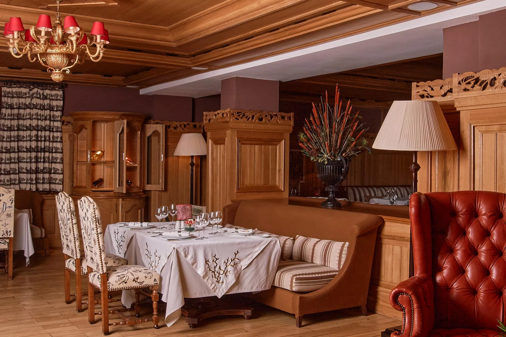 Salle à manger élégante avec table dressée, chandelier, lampes et canapés en cuir