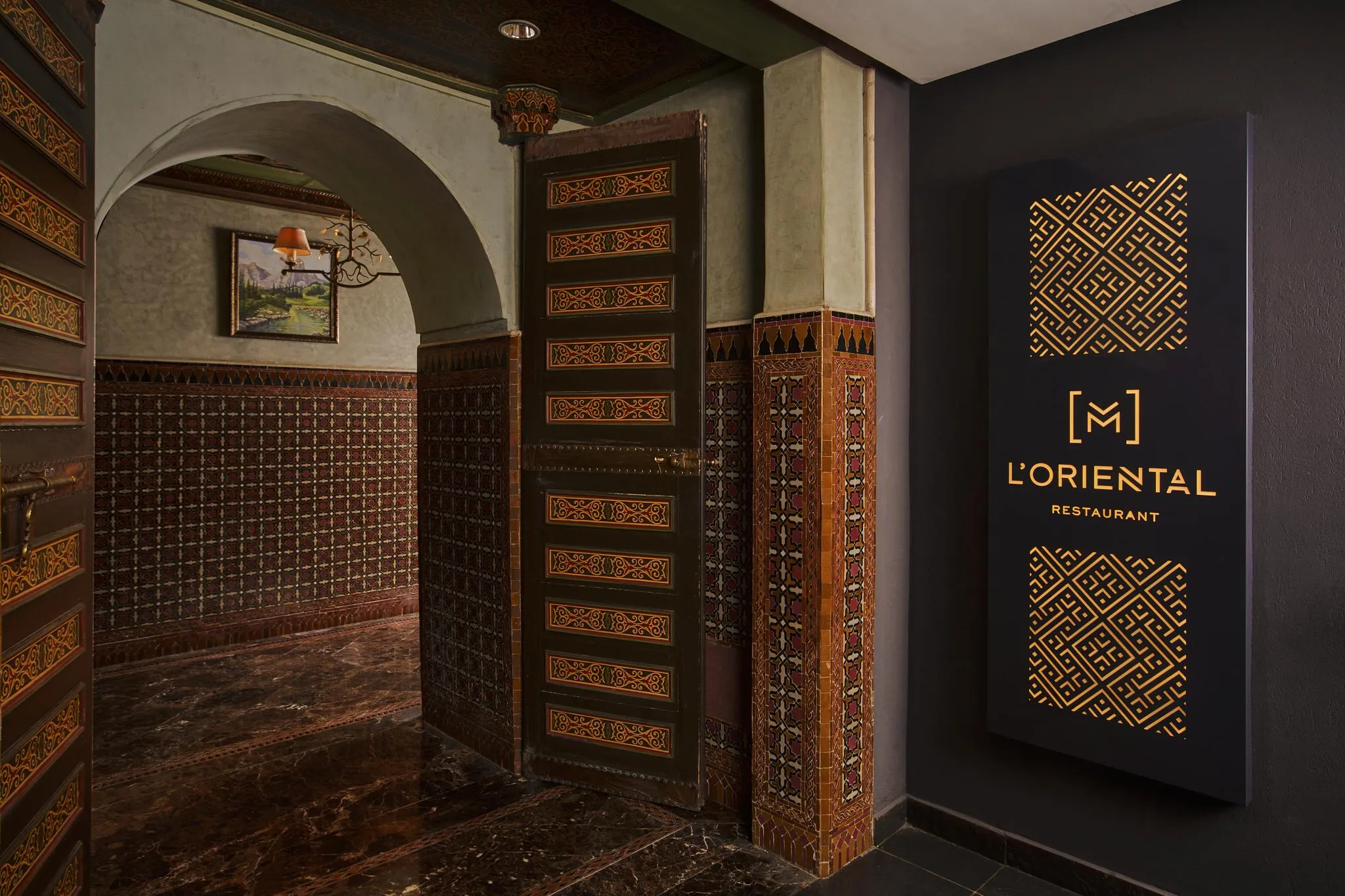 Entrance to a restaurant named L'Oriental with a carved wooden door and a geometric-patterned illuminated sign