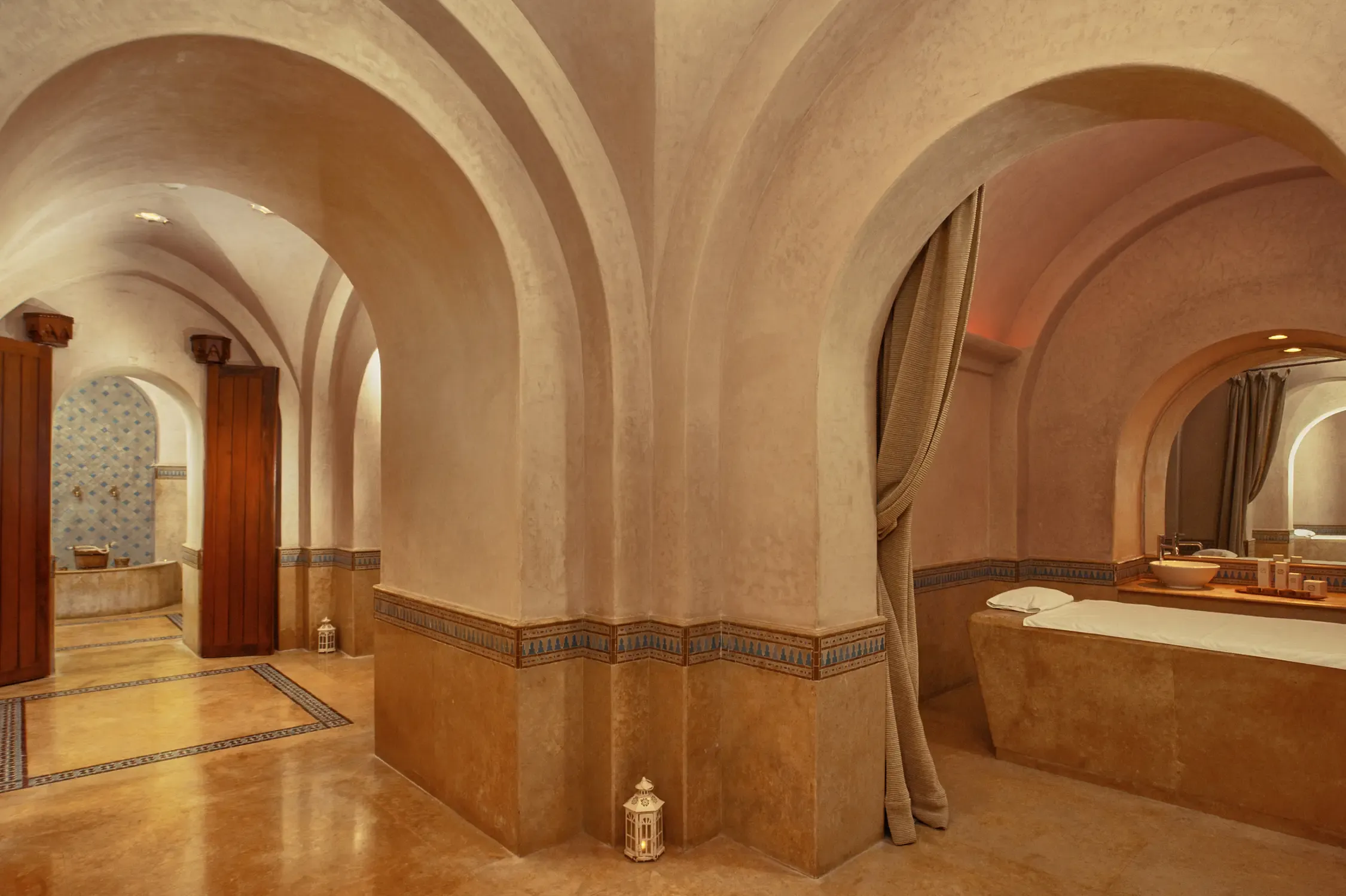 Salle de bain luxueuse avec arches, carrelage beige et motifs décoratifs, contenant des lavabos et une baignoire