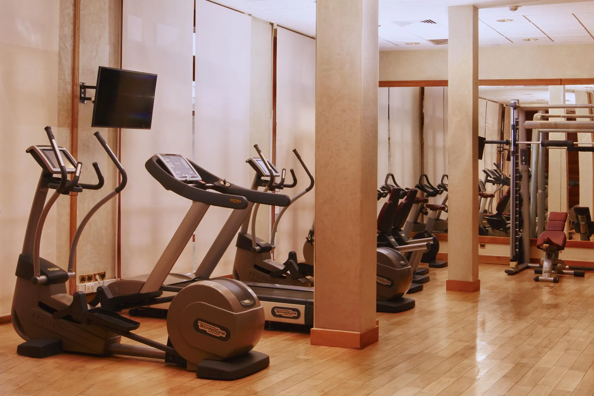 Gym with several cardio-training machines, including ellipticals and bikes, lined up against a wall with mirrors