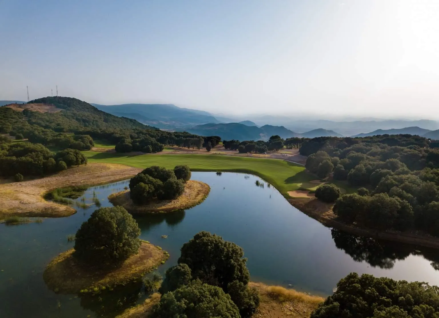 Aerial view of a lake surrounded by trees and hills with golf courses in the background