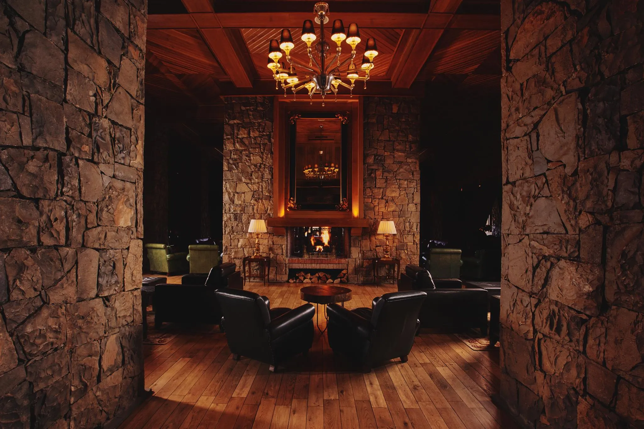 Living room with stone fireplace, chandelier, and leather armchairs around a coffee table